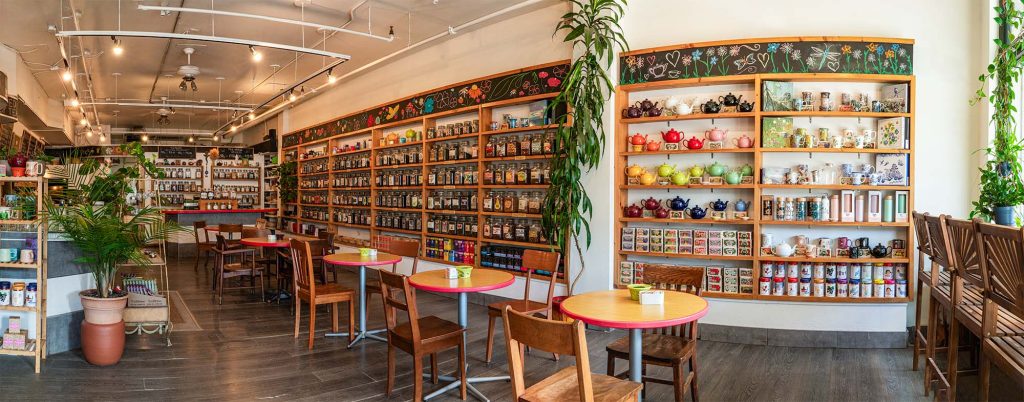 A panoramic view of a stylish tea shop located in Ottawa, featuring a modern and inviting interior with comfortable seating, elegant décor, and a display of various tea blends. The image showcases the warm ambiance and sophisticated design of the space, highlighting the shop’s unique atmosphere and attention to detail.